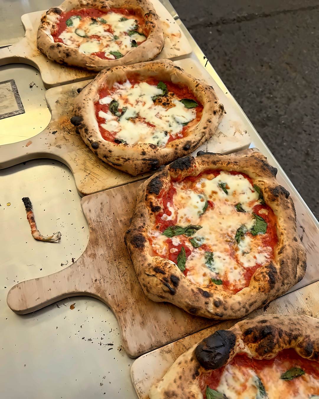 Vier neapolitanische Pizzen mit Leoparding am Rand auf Holzbrettern nach dem Backen im Pizzakurs